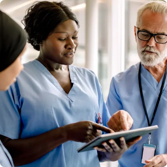 Tre helsepersonell ser på et nettbrett og diskuterer det.