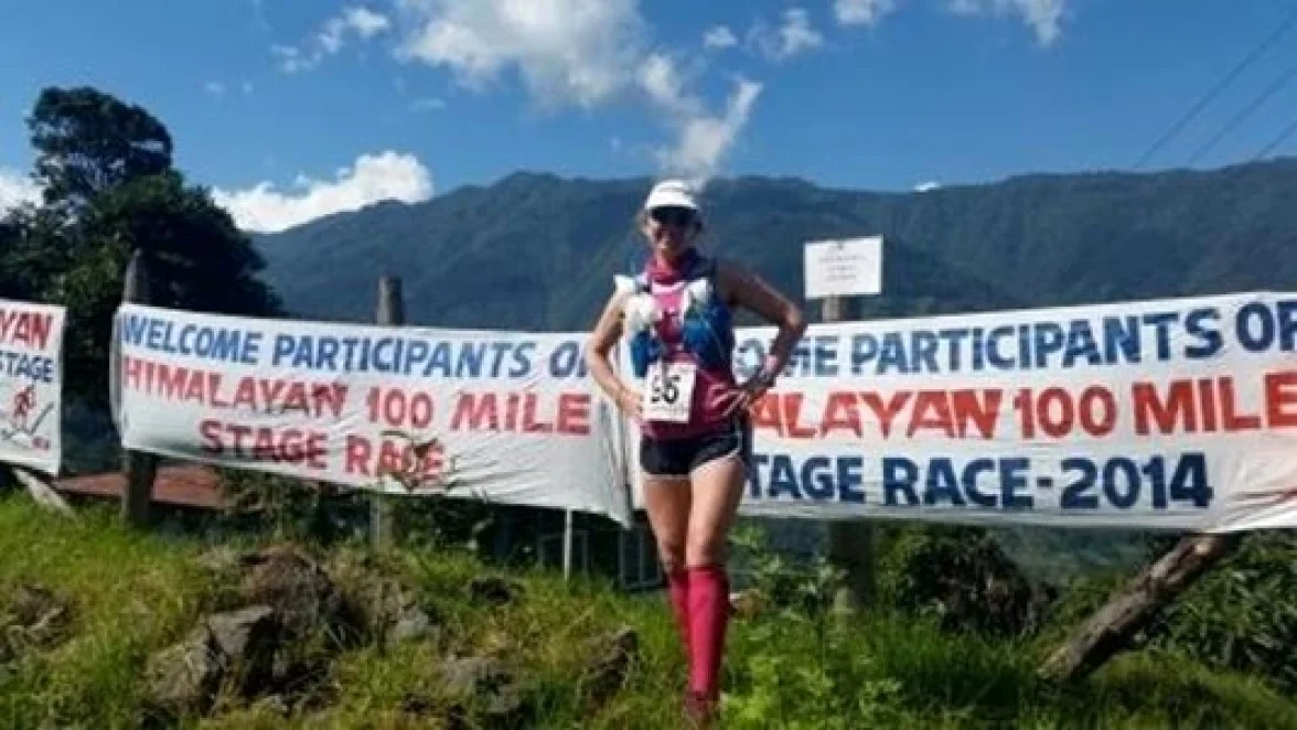 Eine Frau steht neben einem Banner mit der Aufschrift "WILLKOMMEN TEILNEHMER DES HIMALAYAN 100 MILE STAGE RACE - 2014".